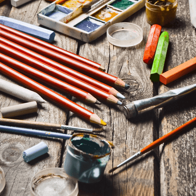 Writing and Drawing | Craftsman Supply Co. (An array of art supplies from pencils to paint to brushes on a wooden table)