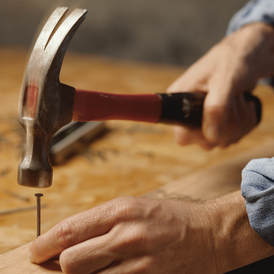 Hammers - Craftsman Supply Co. (Model holding a hammer to hit a nail into a board of wood.)