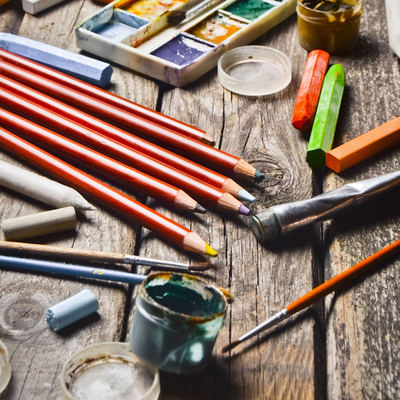 Writing and Drawing | Craftsman Supply Co. (An array of art supplies from pencils to paint to brushes on a wooden table)
