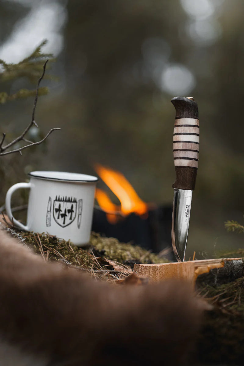 Helle Limited Edition Rein Knife stuck in log beside mug